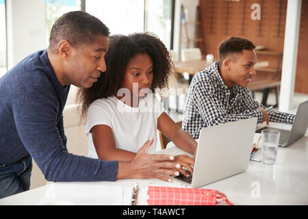Im mittleren Alter schwarzer Mann, der seine Kinder im Teenageralter helfen, ihre Hausaufgaben mit Laptops Stockfoto