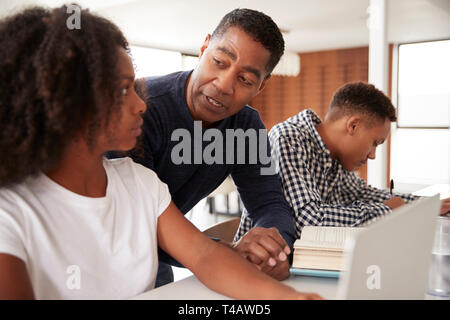 Im mittleren Alter schwarz Dad seiner jugendlich Kind Hilfe bei den Hausaufgaben, niedrigen Winkel, in der Nähe Stockfoto