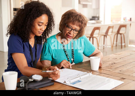 Weibliche healthcare Arbeiter ein Formular mit einer älteren Frau, die während einer Home Gesundheit besuchen Sie Stockfoto
