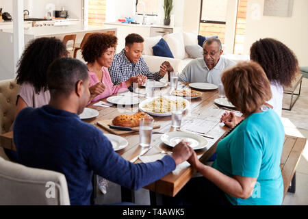 Drei generation schwarze Familie am Tisch halten sich an den Händen und sagen Gnade vor dem Essen sitzen Stockfoto