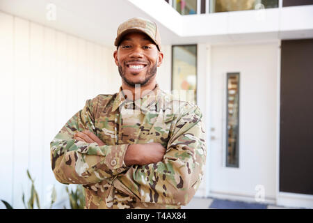 Soldat in der Tarnung außerhalb modernes Haus mit gekreuzten Armen lächelnd in die Kamera, in der Nähe Stockfoto