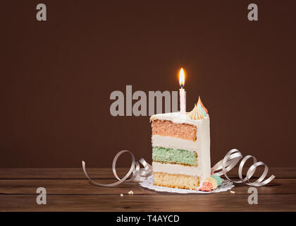 Birthday Cake Slice mit drei pastellfarbenen Schichten und Kerzenlicht auf braunem Hintergrund Stockfoto