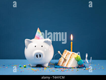 Stück Kuchen mit einer Kerze und Piggy Bank über einen blauen Hintergrund. Geburtstag Geld Konzept. Stockfoto