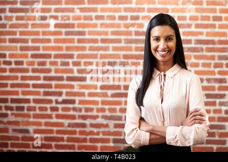 Portrait von lächelnden Jungen Geschäftsfrau Stehend gegen Mauer in modernen Büro Stockfoto
