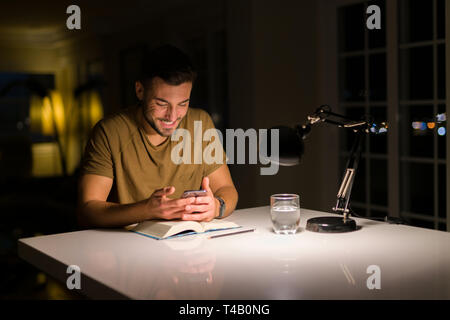 Jungen gutaussehenden Mann zu Hause studieren, mit Smartphone, suchen am Telefon lächeln Stockfoto