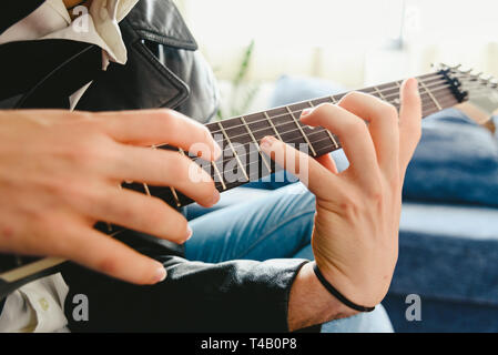 Junger Mann, der mit seiner E-Gitarre auf dem Sofa seines Hauses lernen. Stockfoto