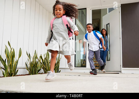 Aufgeregte Kinder laufen aus der vorderen Tür auf dem Weg in die Schule beobachtet von Mutter Stockfoto