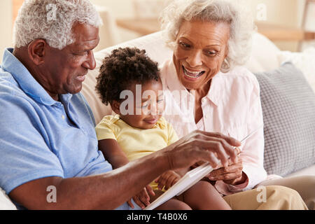 Großeltern Sitzen auf einem Sofa zu Hause lesen Buch mit Baby Enkelin Stockfoto