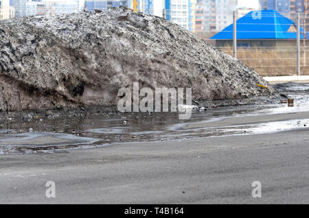 Haufen schmutziger Schnee auf einem Parkplatz mit Pfützen und Müll gesammelt über Winter. Warmen Frühlingstag Stockfoto