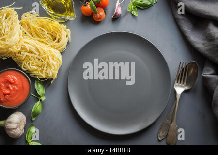 Leere schwarze Platte und Grenze der rohen Pasta, Tomaten im eigenen Saft, Basilikum, Parmesan zum Kochen italienische und mediterrane Gerichte. Stockfoto