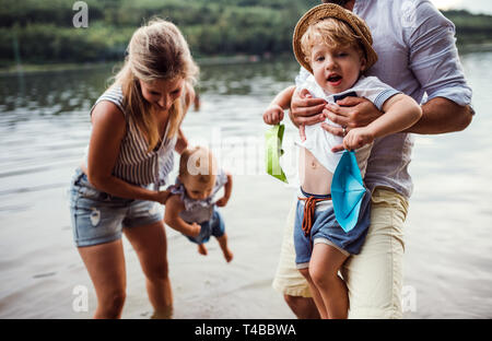 Eine junge Familie mit 2 Kleinkind Kinder draußen am Fluss im Sommer. Stockfoto