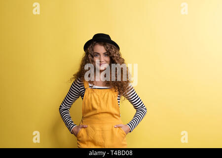 Porträt einer jungen Frau mit schwarzem Hut in einem Studio auf einem gelben Hintergrund. Stockfoto