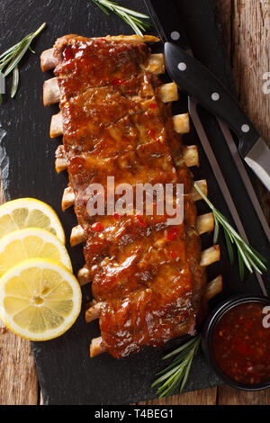 Frisch gegrillte Schweinerippchen mit Chili Sauce und Zitrone close-up vorbereitet auf einer Schiefertafel Board auf dem Tisch. Vertikal oben Ansicht von oben Stockfoto