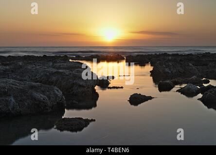 Sonnenaufgang über dem Mittelmeer mit schönen Himmel und felsigen Pools reflektieren die Sonnenstrahlen im Vordergrund, Cala Bona, Mallorca, Spanien. Stockfoto