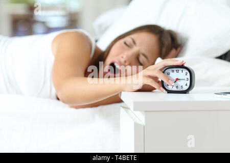 Müde Frau Gähnen bei Wakeup ausschalten Wecker auf einem Bett zu Hause liegen Stockfoto