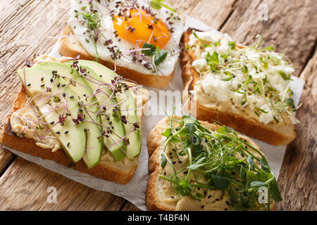 Satz von verschiedenen Toasts mit Hummus, Avocado, Fetakäse, microgreen und ei Nahaufnahme auf dem Tisch. Horizontale Stockfoto