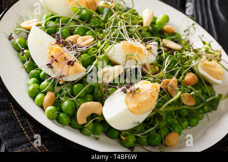 Leckeren, gesunden Salat von grünen Erbsen, micro Grüns, Nüsse und Eier close-up auf einem Schild auf dem Tisch gekocht. Horizontale Stockfoto