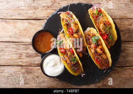 Lecker gefüllte Tacos mit glasierten Huhn, microgreen und Gemüse mit Saucen in der Nähe serviert auf einem Schiefer Board auf dem Tisch. Horizontale Ansicht von oben Stockfoto