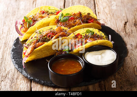 Mexikanischen fast food Tacos mit glasierten Huhn, microgreen und Gemüse mit Saucen in der Nähe serviert auf einem Schiefer Board auf dem Tisch. Horizontale Stockfoto
