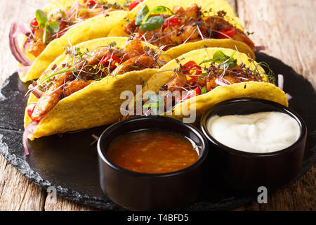 Authentische Tacos mit glasierten Huhn, microgreen und Gemüse sind mit Saucen in der Nähe serviert auf einem Schiefer Board auf dem Tisch. Horizontale Stockfoto