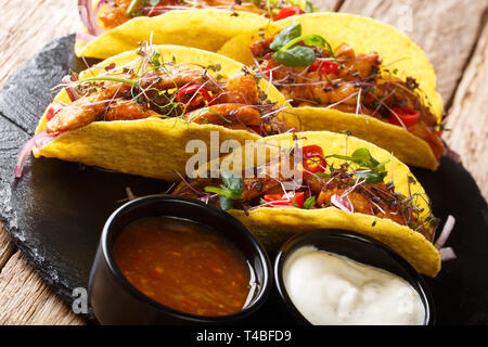 Lecker gefüllte Tacos mit glasierten Huhn, microgreen und Gemüse mit Saucen in der Nähe serviert auf einem Schiefer Board auf dem Tisch. Horizontale Stockfoto