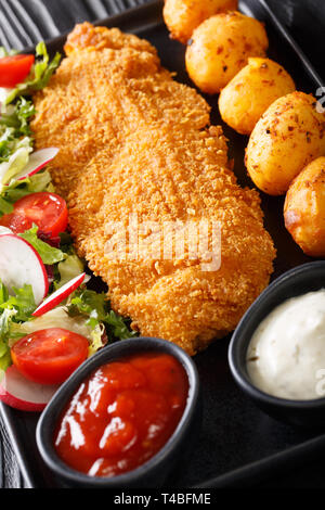 Kabeljaufilet in Panade mit jungen Kartoffeln und frischem Gemüse Salat close-up auf einem Teller auf den Tisch. Vertikale Stockfoto