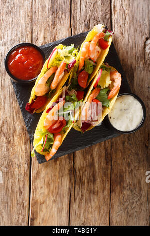 Knusprige mais Tacos mit Meeresfrüchten frisch Gemüse und Saucen close-up auf den Tisch. Vertikal oben Ansicht von oben Stockfoto