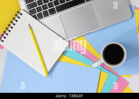 Flach Foto eines kreativen Arbeitsplatz. Blick von oben auf einen Schreibtisch mit bunten Pastell Papier, Notizblock und Bleistift, Laptop und Kaffee Tasse mit kopieren. Stockfoto