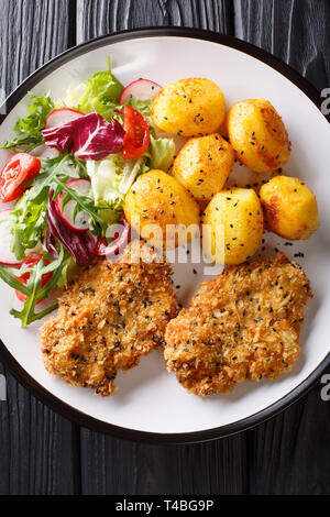 Dienen gebratene Steaks in Sesam Panieren mit neuen Kartoffeln und frischem Salat close-up auf einem Teller auf den Tisch. Vertikal oben Ansicht von oben Stockfoto