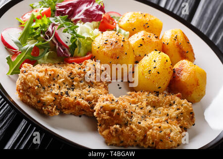 Dienen gebratene Steaks in Sesam Panieren mit neuen Kartoffeln und frischem Salat close-up auf einem Teller auf den Tisch. Horizontale Stockfoto