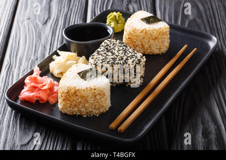 Dreieckige onigiri mit Sesam mit Ingwer, Wasabi und Sojasauce in der Nähe serviert auf einem Teller auf den Tisch. Horizontale Stockfoto