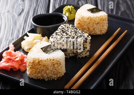 Teil von onigiri dreieckige Rollen in Sesam mit Ingwer, Wasabi und Sauce in der Nähe serviert auf einem Teller auf den Tisch. Horizontale Stockfoto
