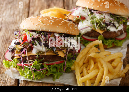 Rindfleisch Burger mit frischem Gemüse, microgreen, Cheddar Käse und Sauce serviert mit Pommes frites Close-up auf dem Tisch. Horizontale Stockfoto