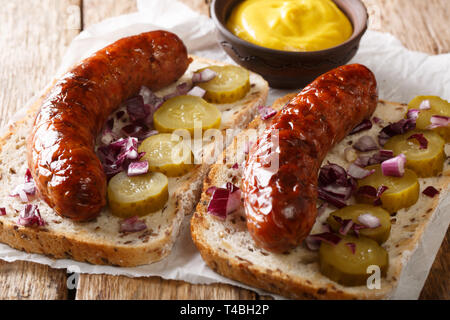 Leckere Toasts mit gegrillten Würstchen, Gewürzgurken, Zwiebeln und Senf close-up auf dem Tisch. Horizontale Stockfoto