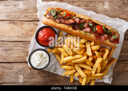 Landhausstil Hot Dog mit Speck und Gemüse mit Pommes frites und Saucen in der Nähe serviert - auf den Tisch. horizontal oben Ansicht von oben Stockfoto