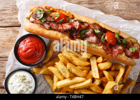 Lecker Hot Dog mit Speck und Gemüse mit Pommes frites und Saucen in der Nähe serviert - auf den Tisch. horizontal oben Ansicht von oben Stockfoto