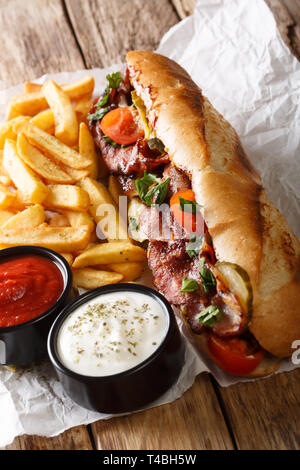 Lecker Hot Dog mit Speck und Gemüse mit Pommes frites und Saucen in der Nähe serviert - auf den Tisch. Vertikale Stockfoto