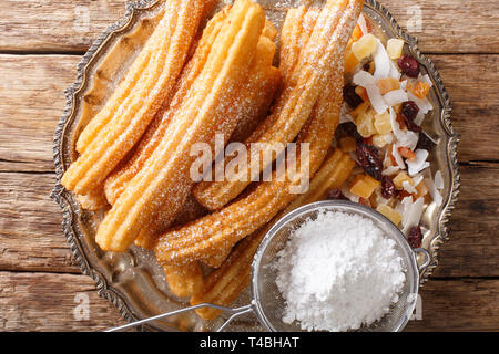 Churros sind goldgelb und knusprig gebratener Gebäck mit Zuckerbestreuter Pulver close-up auf einem Teller auf den Tisch. horizontal oben Ansicht von oben Stockfoto