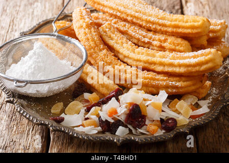 Hochkalorische frittierten Churros mit Puderzucker und kandierten Früchten close-up auf einem Teller auf den Tisch. Horizontale Stockfoto