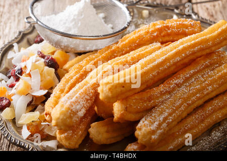 Frisch heiß Churros mit Puderzucker und kandierten Früchten close-up auf dem Tisch gemacht. Horizontale Stockfoto