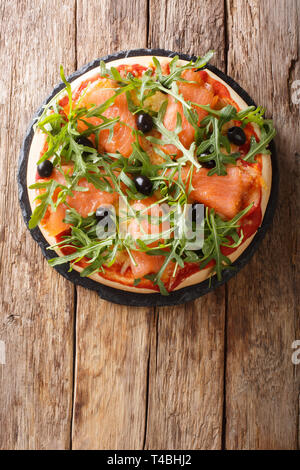 Rezept für köstliche italienische Pizza mit Lachs und Rucola, schwarze Oliven und Mozzarella close-up auf den Tisch. Vertikal oben Ansicht von oben Stockfoto