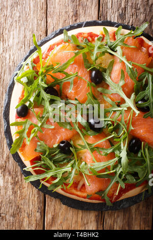 Leckere Pizza mit gesalzenen Lachs, Rucola, Oliven und Käse Nahaufnahme auf dem Tisch. Vertikal oben Ansicht von oben Stockfoto