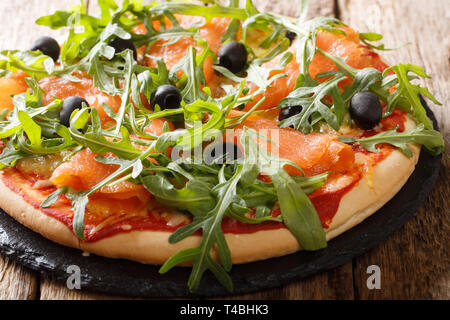 Lachs Pizza mit frischem Rucola, schwarze Oliven und Käse Nahaufnahme auf dem Tisch. Horizontale Stockfoto