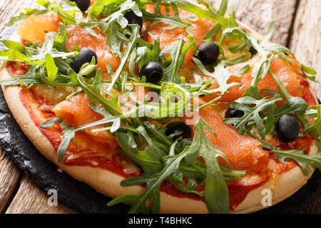 Knusprige Pizza mit gesalzenen Lachs, frischem Rucola, Oliven und Käse Nahaufnahme auf dem Tisch. Horizontale Stockfoto