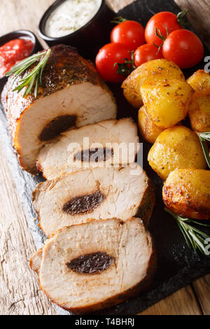 Gebackenes Schweinefleisch mit Pflaumen mit jungen Kartoffeln und Saucen in der Nähe serviert - auf den Tisch. Vertikale Stockfoto