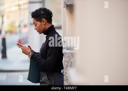 Junge schwarze Frau, die auf einer Straße in London können Sie über ihr Smartphone, Seitenansicht, Nahaufnahme, selektiven Fokus Stockfoto