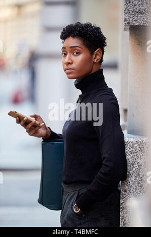 Junge erwachsene Frau auf einer Straße in London stehen mit ihrem Smartphone und Wegsehen, selektiver Fokus Stockfoto