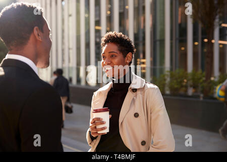 Junge schwarze Geschäftsfrau stehen auf der Straße mit einem Takeaway Kaffee, Gespräch mit ihr männlicher Kollege, selektiver Fokus Stockfoto