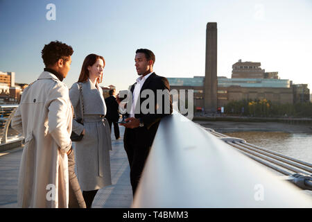 Seitenansicht von drei tausendjährigen Kollegen stehen mit Millennium Bridge, London, selektiven Fokus Stockfoto