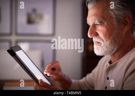 Senior Hispanic Mann an einem Tisch sitzen mit einem Tablet Computer am Abend, Nahaufnahme, Seitenansicht Stockfoto